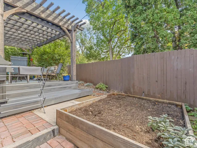 Wood pergola over a multi-level deck, featuring a raised garden bed and brick paver patio