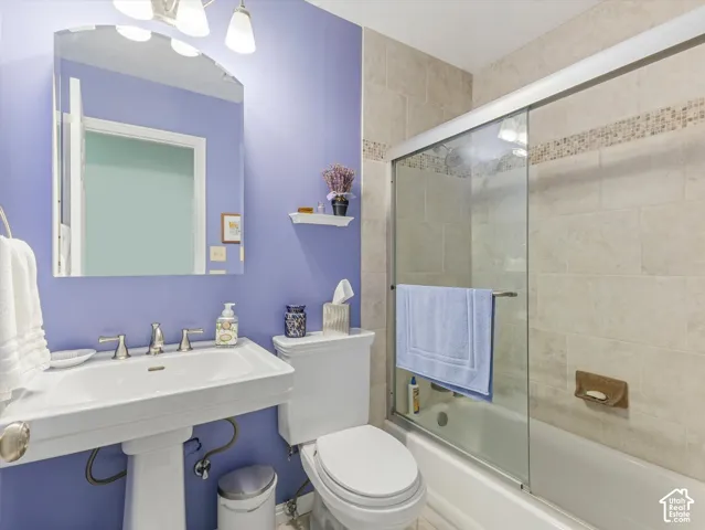 Pedestal sink with chrome fixtures, tiled shower surround with mosaic accent, sliding glass shower door, and three-light vanity fixture