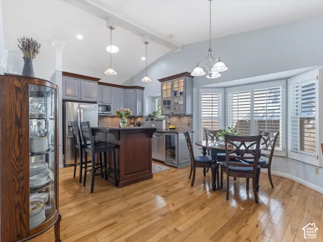 Kitchen featuring wood-finish flooring, vaulted ceiling with exposed beams, stainless steel appliances, kitchen island with seating, and a dining area with bay windows