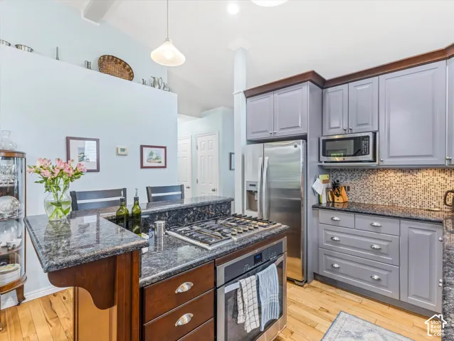 Kitchen featuring light wood-finish flooring, two-tone cabinetry with gray upper and dark wood lower cabinets, dark granite countertops, and a tile backsplash