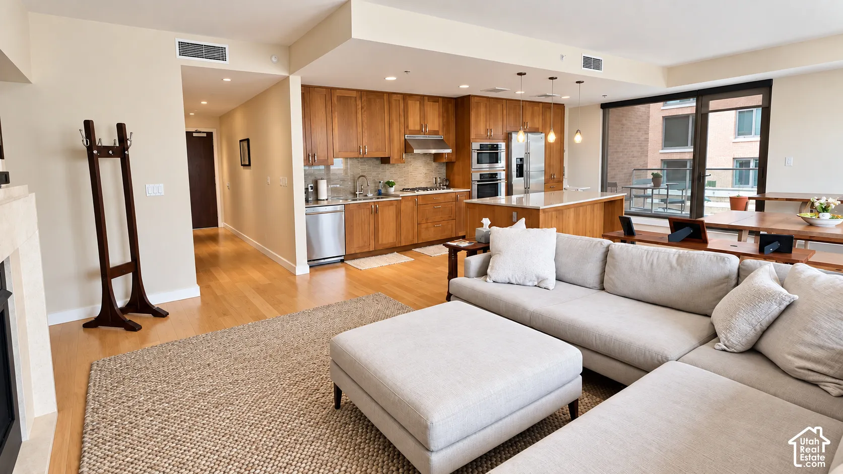 Open-concept living area with wood-finish flooring, a kitchen featuring wood cabinetry and stainless steel appliances, and an island with countertop seating