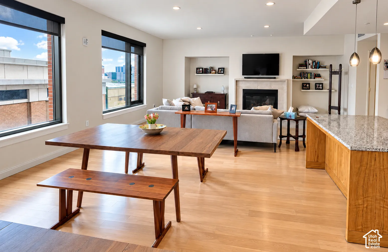 Bright living area featuring wood-finish flooring, a fireplace with a stone surround, and recessed lighting