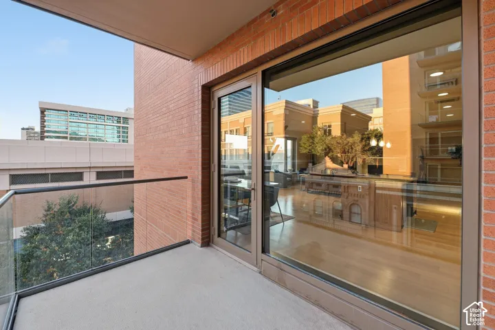 Exterior balcony featuring a concrete floor, glass railing, and brick wall