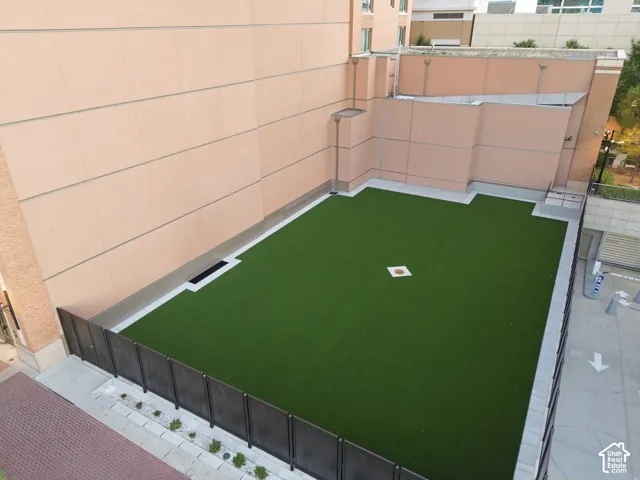 Expansive artificial turf area with perimeter fencing, surrounded by neutral-toned building facades and a hardscape border