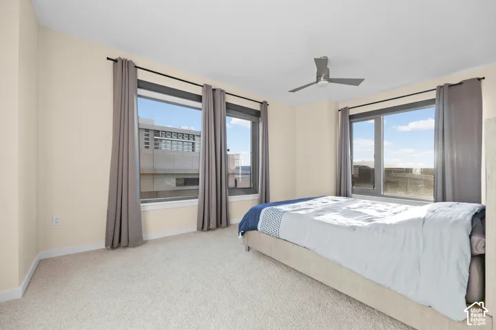 Expansive windows providing abundant natural light, neutral wall colors, carpet flooring, and a ceiling fan