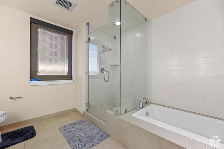 Glass-enclosed shower with subway tile surround, separate soaking tub, and tile flooring