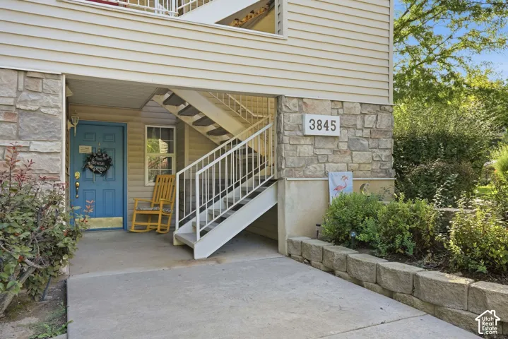Stone facade with siding accents, concrete entryway, exterior staircase, and mature perimeter landscaping