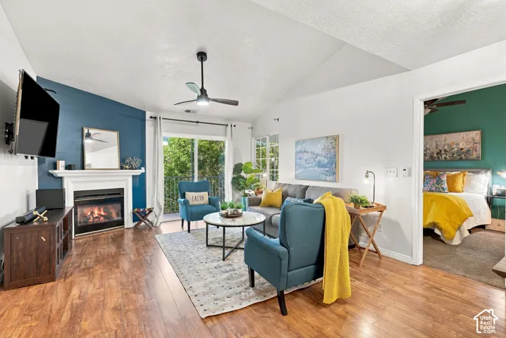 Living area featuring vaulted ceilings, wood-finish flooring, a fireplace with a white mantel, a ceiling fan, and sliding glass door access to an outdoor area