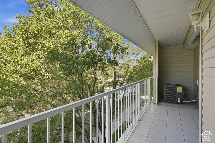 Balcony featuring a tiled floor, white railing, and exterior wall light fixture