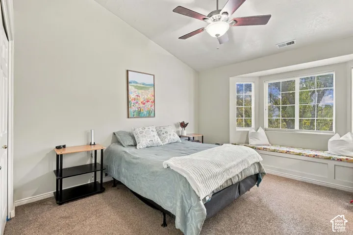 Vaulted ceiling with a ceiling fan, carpeted flooring, and a built-in window seat with storage