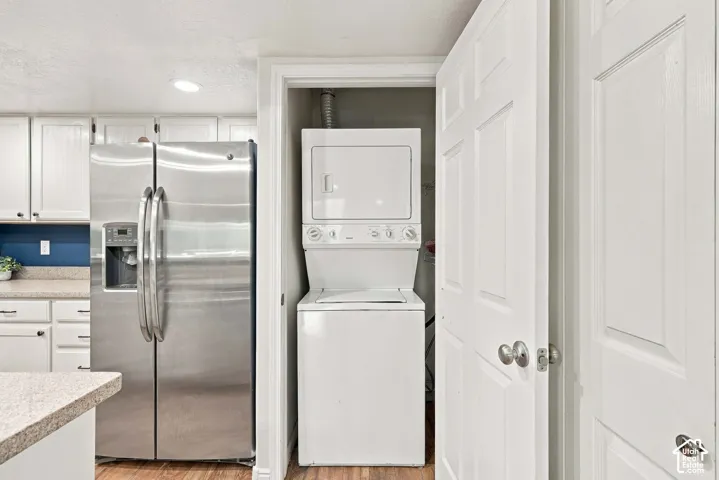 White cabinetry, stainless steel refrigerator with ice dispenser, wood-finish flooring, and a stacked washer and dryer unit