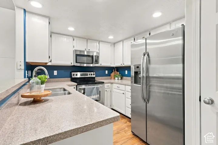 Modern kitchen featuring white cabinetry, stainless steel appliances including a French-door refrigerator and gas range, quartz countertops with contrasting edge banding, a deep undermount sink, recessed lighting, and a striking navy blue tile backsplash