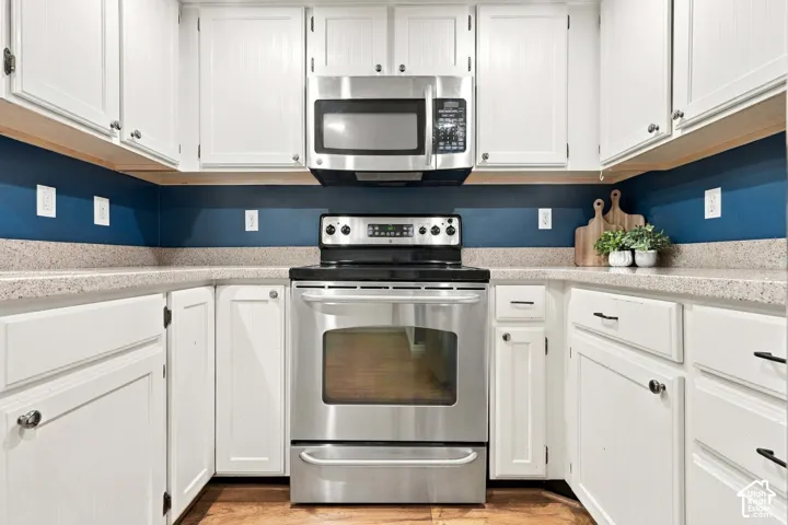 White cabinetry, stainless steel appliances, speckled countertops, and a built-in microwave