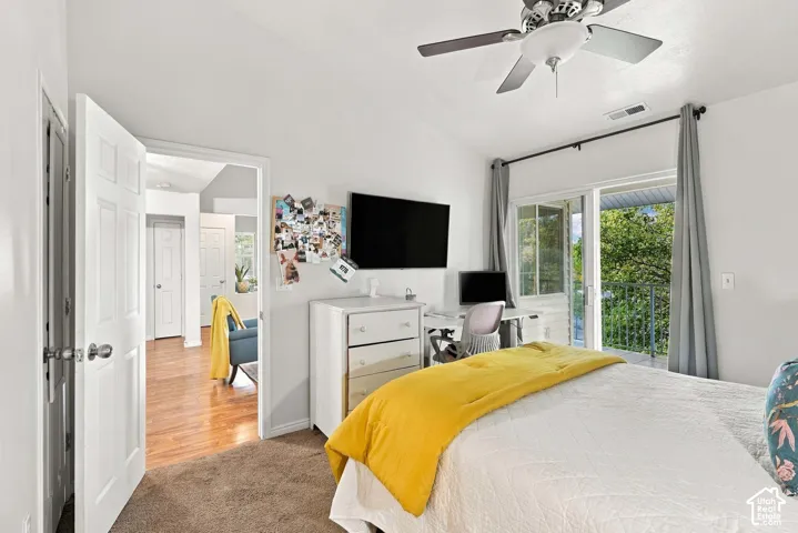 Carpeted flooring, vaulted ceiling, ceiling fan, sliding glass door leading to a balcony, and a built-in wall-mounted television