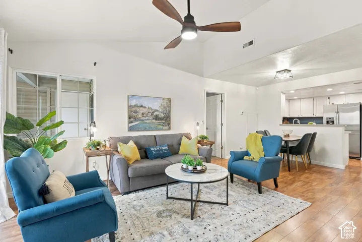 Vaulted ceiling with a ceiling fan, wood-finish flooring, and a kitchen with white cabinetry and stainless steel appliances