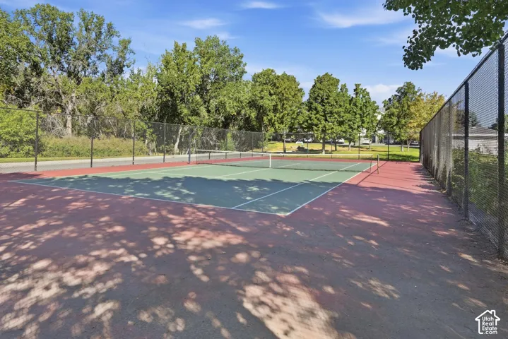 Hard surface tennis court featuring a green playing area, red surrounding court, and black chain-link fencing