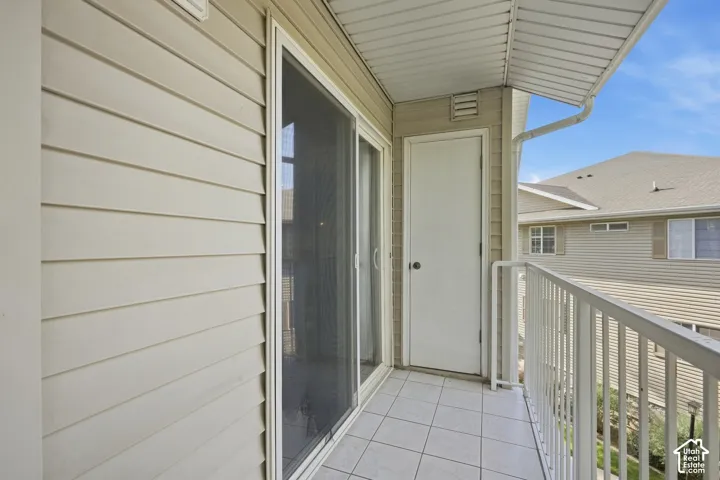 Balcony featuring tiled flooring, a sliding glass door, white railing, and a solid exterior door