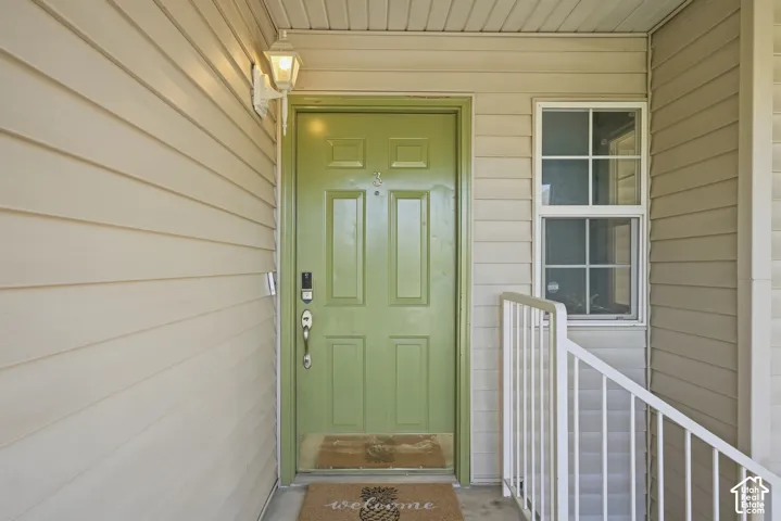 Light-colored siding exterior with a green panel door, featuring a wall-mounted light fixture, and a window with grid inserts