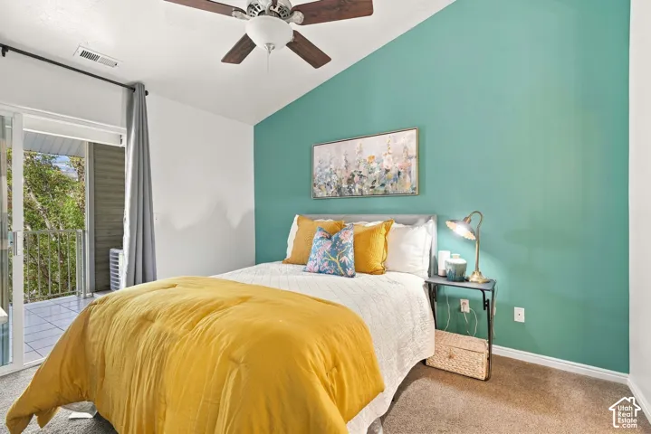 Vaulted ceiling with a ceiling fan, sliding glass door access to a private balcony, and plush carpet flooring