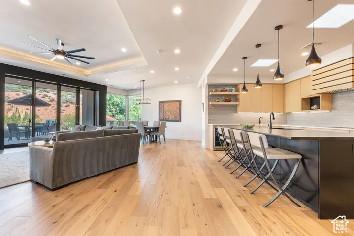 Open-concept living area featuring wood-finish flooring, a contemporary kitchen island with seating, recessed lighting, and expansive glass sliding doors