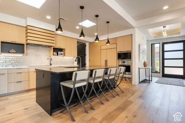 Gourmet kitchen featuring wood-finish flooring, custom cabinetry, a large island with seating, integrated appliances, and a subway tile backsplash