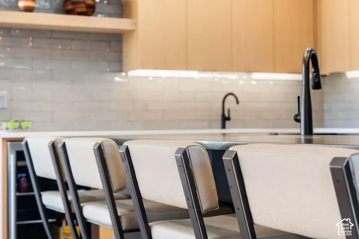 Light wood-finish cabinetry, gray subway tile backsplash, matte black fixtures, and under-cabinet lighting