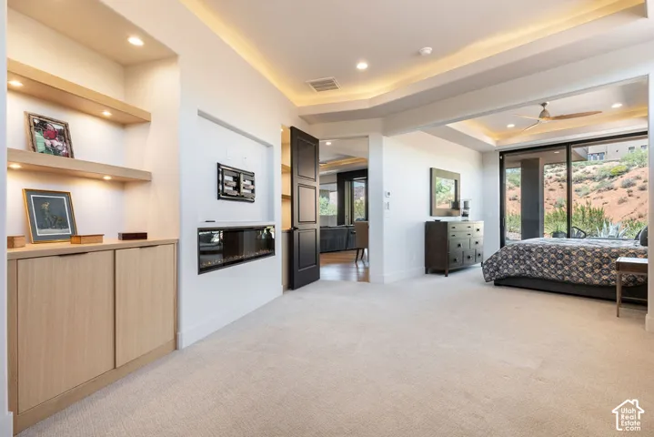 Built-in shelving with integrated lighting, wall-mounted electric fireplace, recessed ceiling lighting, tray ceiling design, and a large sliding glass door