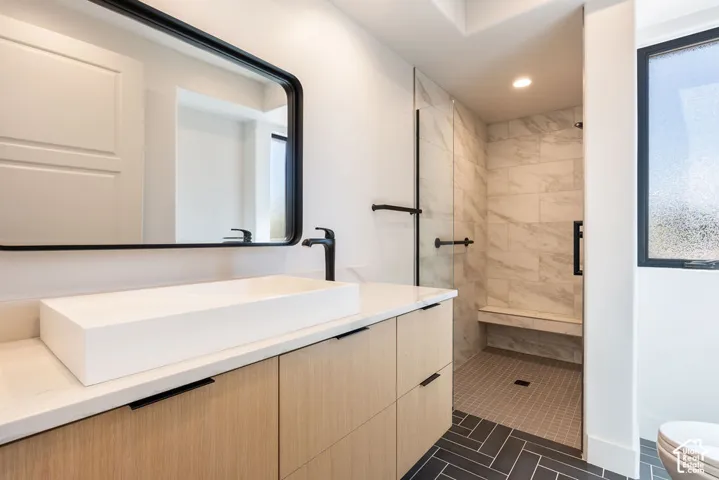Vanity with a rectangular vessel sink and matte black faucet, tile flooring, walk-in shower with a built-in bench, and a textured privacy window