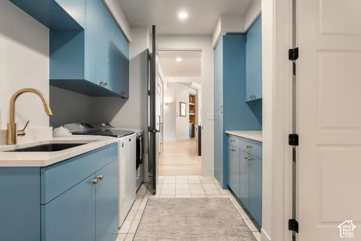 Laundry area featuring blue cabinetry, a built-in sink with a gold-finish faucet, and light-toned tile flooring. There is direct access to the primary suite from this room.