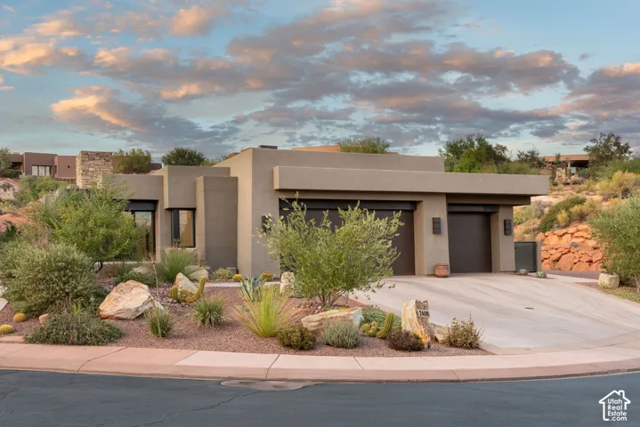 Contemporary exterior with stucco finish, integrated garage doors, stone accents, desert landscaping, and a concrete driveway