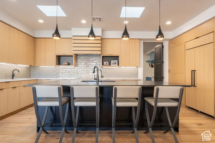 Modern kitchen featuring wood-finish cabinetry, a large kitchen island with counter seating, a subway tile backsplash, and recessed and pendant lighting