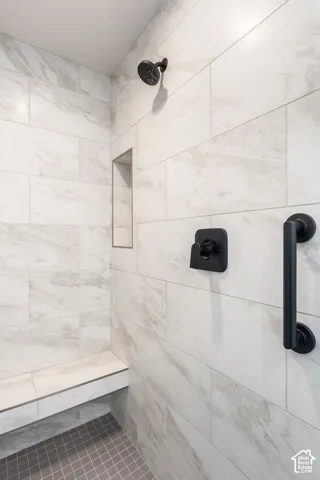 Shower with light-toned tiled walls, a built-in shower bench, and dark-toned hardware