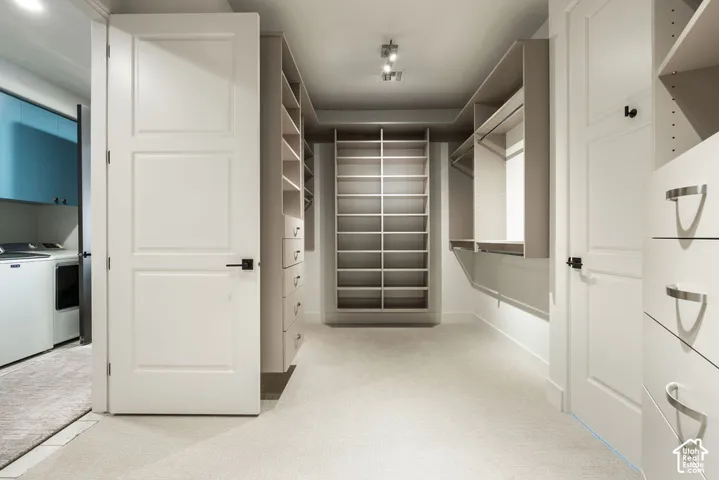 Spacious walk-in closet featuring a doorway to the laundry and extensive built-in shelving, hanging rods, and integrated drawers with contemporary hardware