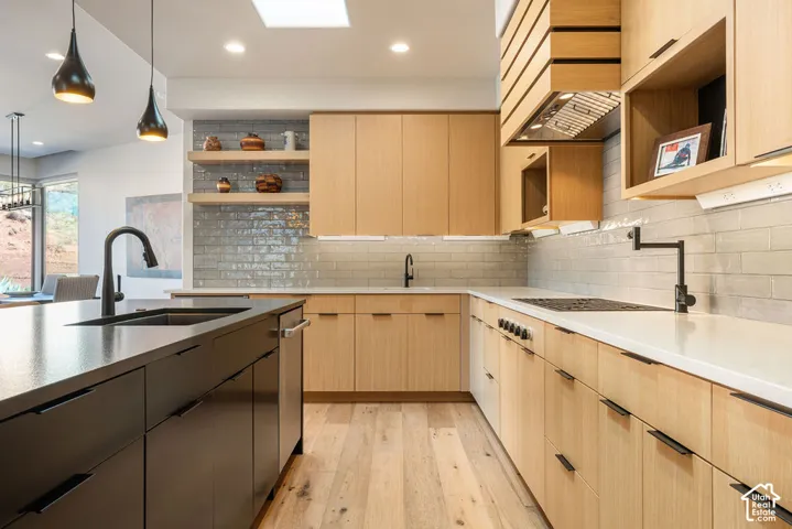 Modern kitchen with light wood-finish cabinetry, a dark kitchen island, light brick-patterned tile backsplash, a built-in cooktop, and a pot filler