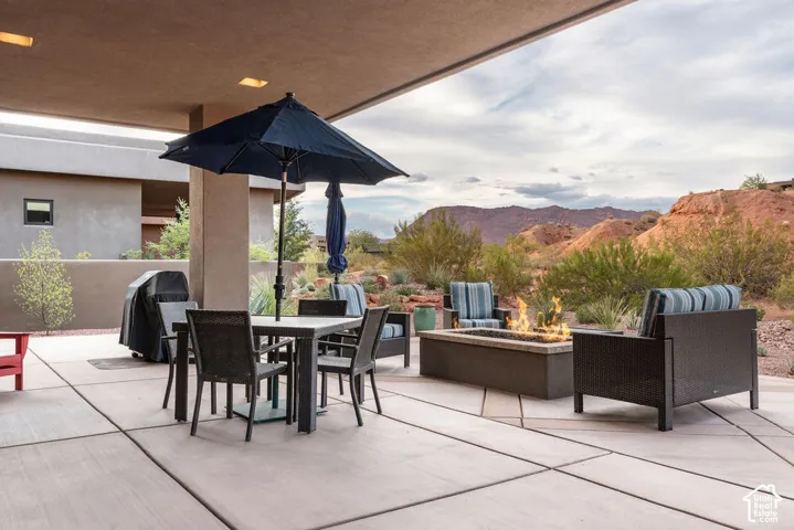 Expansive covered patio featuring large format concrete pavers, a built-in fire pit, and distant mountain scenery