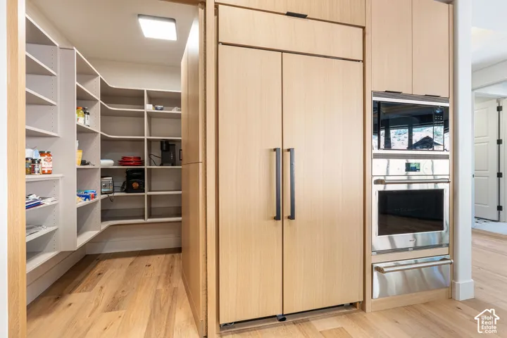 Built-in refrigerator with wood-finish paneling, integrated microwave, built-in oven, and a spacious hidden walk-in pantry with extensive shelving