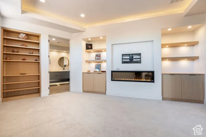 Built-in shelving, recessed lighting, integrated electric fireplace, wood-finish cabinetry, and light-toned carpet