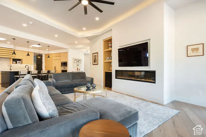 Recessed ceiling lighting, tray ceiling, built-in shelving, linear electric fireplace, and wood-finish flooring