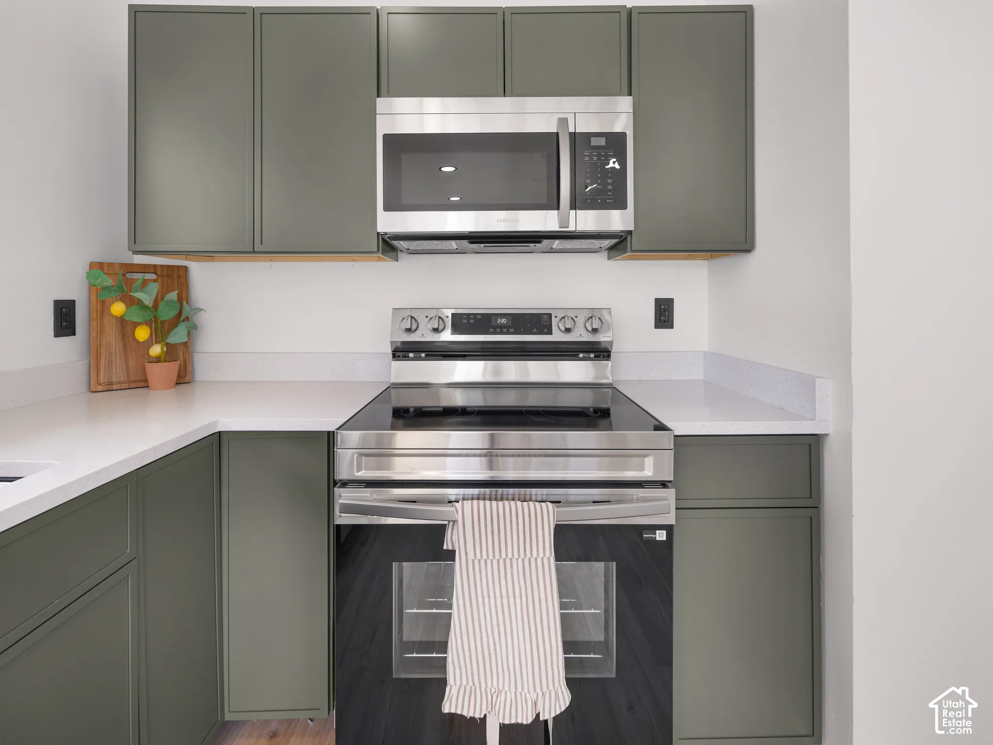 Kitchen featuring sleek green cabinetry, white countertops, stainless steel microwave, and a black cooktop oven