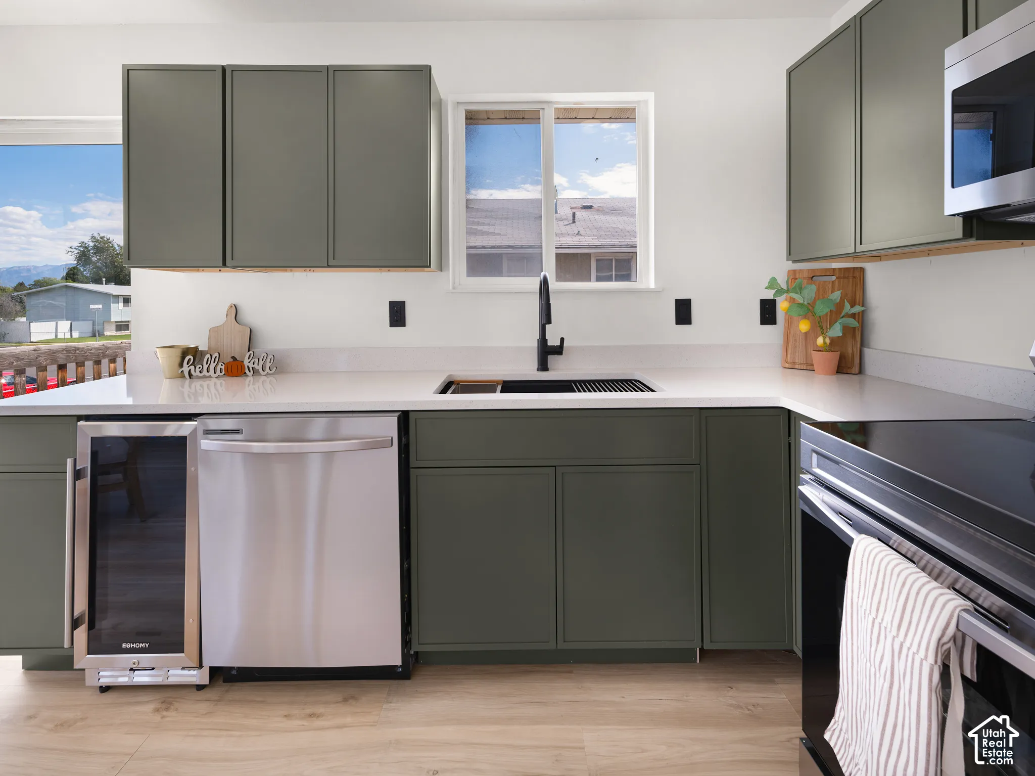 Kitchen featuring olive-toned cabinetry, light-toned countertops, wood-finish flooring, a stainless steel dishwasher, and a built-in beverage refrigerator