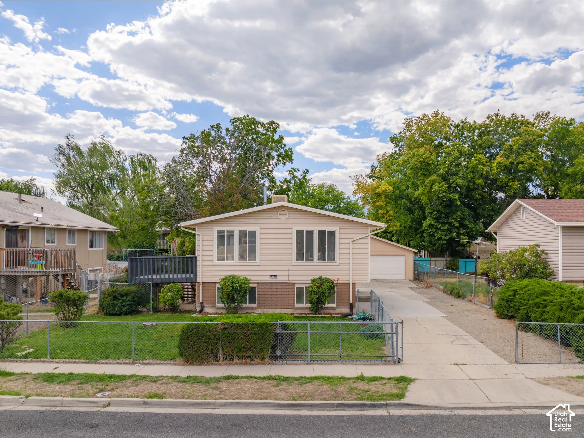 Split-level residence featuring a neutral-toned exterior, an attached garage, a paved driveway, and mature landscaping
