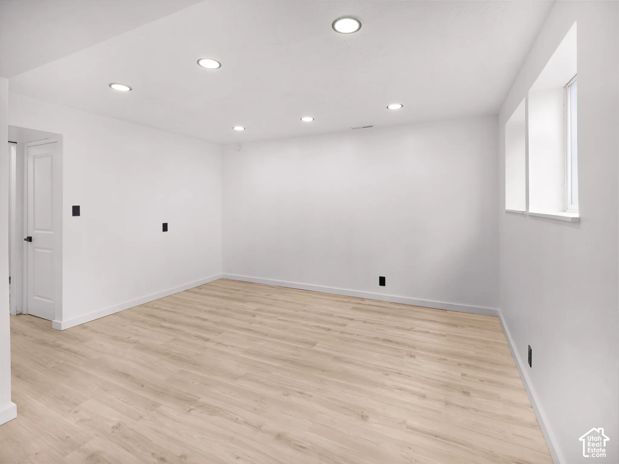 Recessed ceiling lighting, wood-finish flooring, white walls, and a window