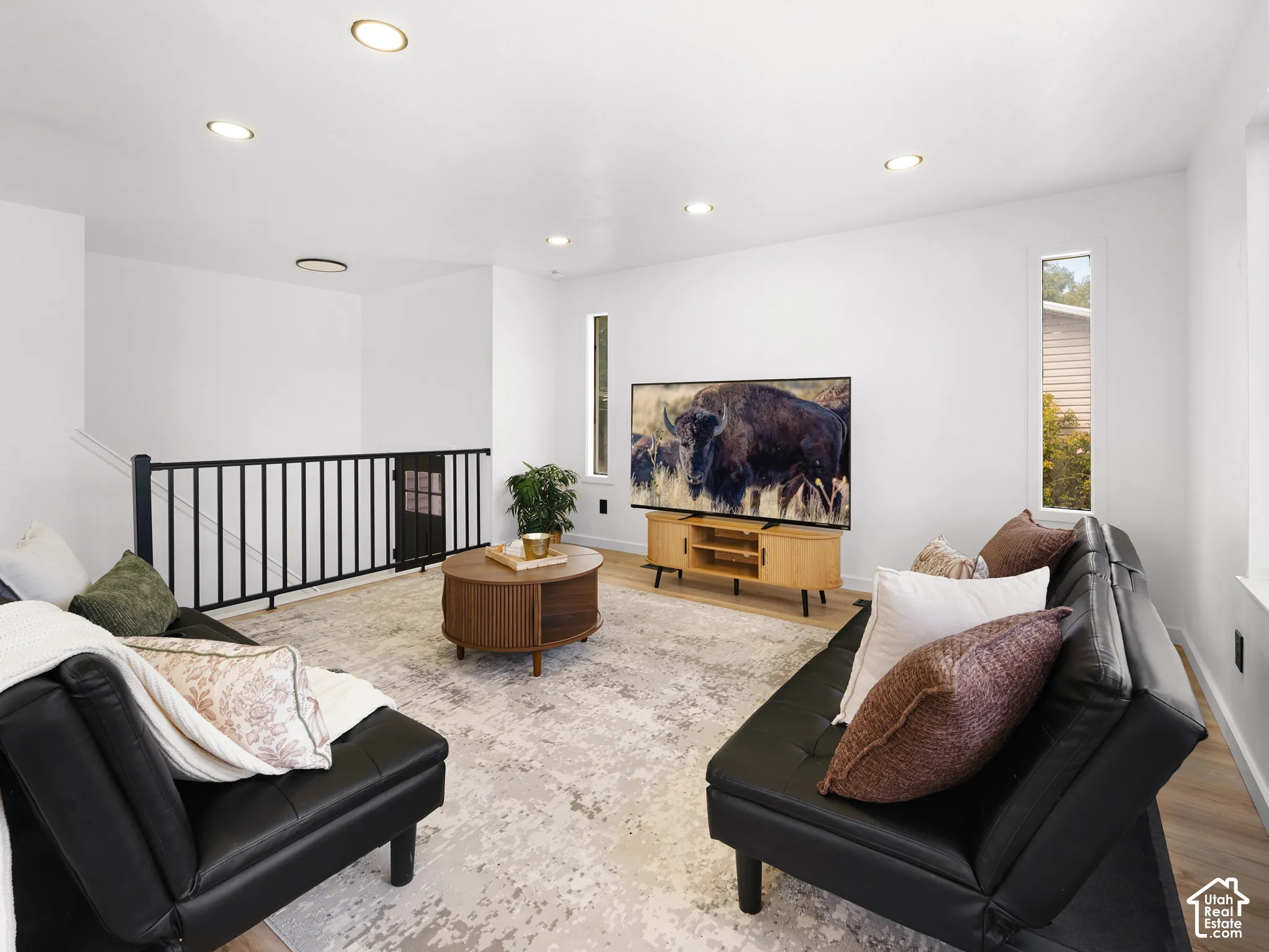 Recessed ceiling lighting, wood-finish flooring, white wall finishes, black metal railing, and a window with vertical orientation