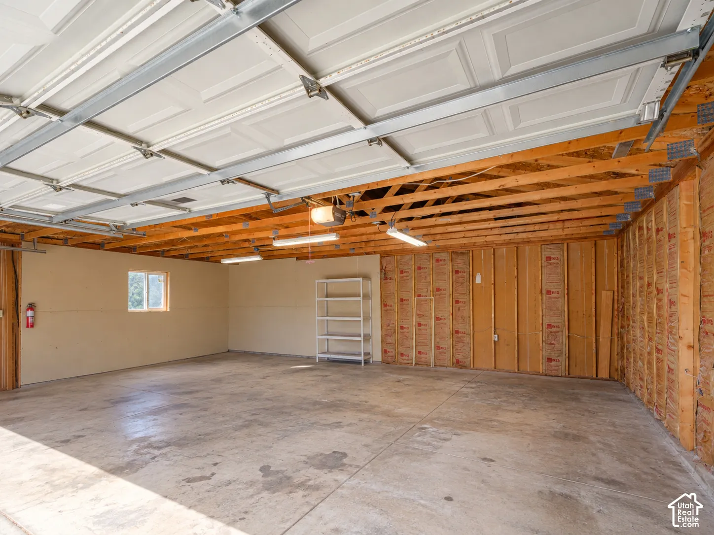 Two garage doors with panel detailing, exposed wood joists, concrete flooring, and a single window
