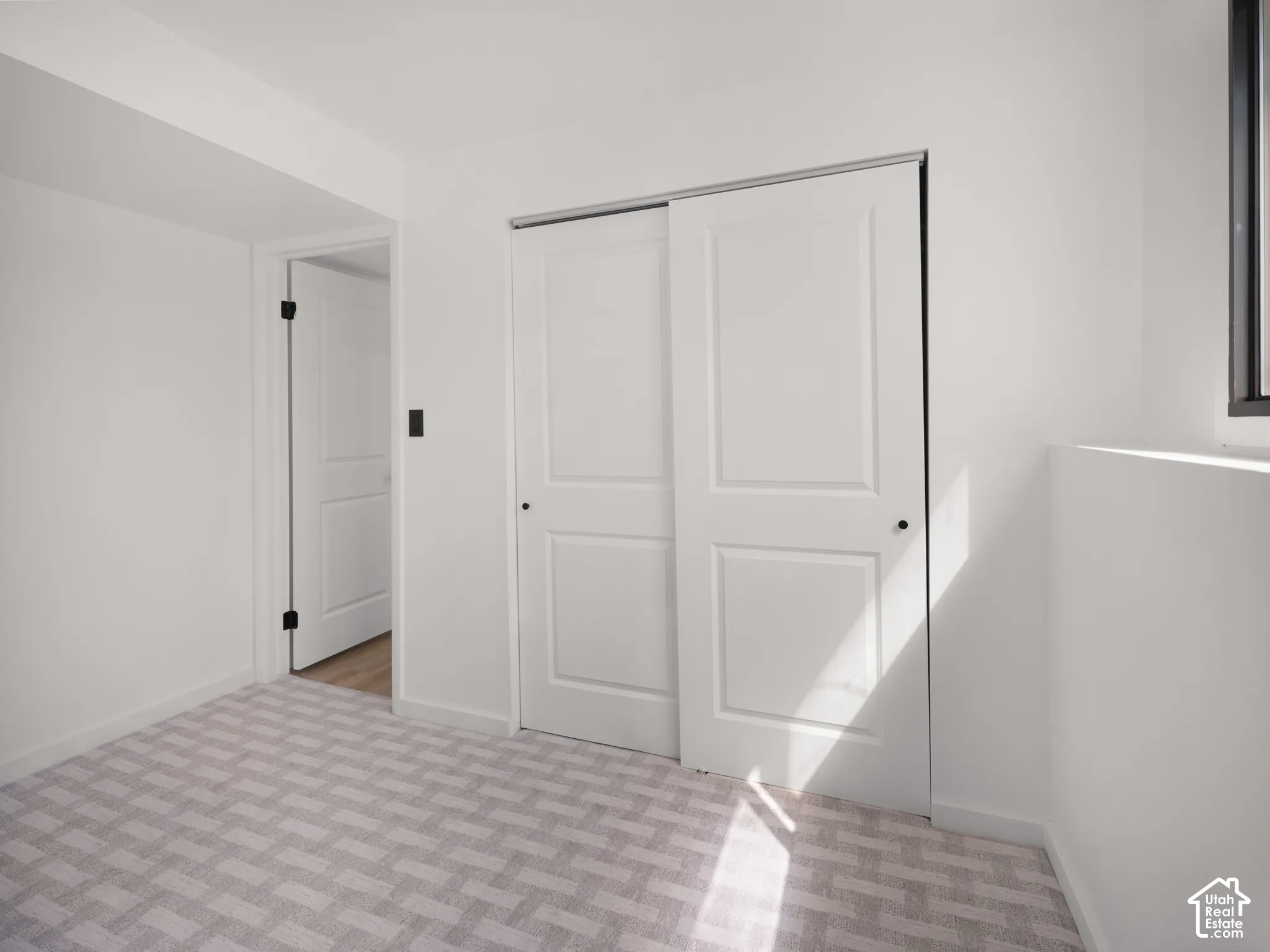 Neutral tone wall paint, light-colored patterned carpet, white sliding closet doors, and a black-framed window