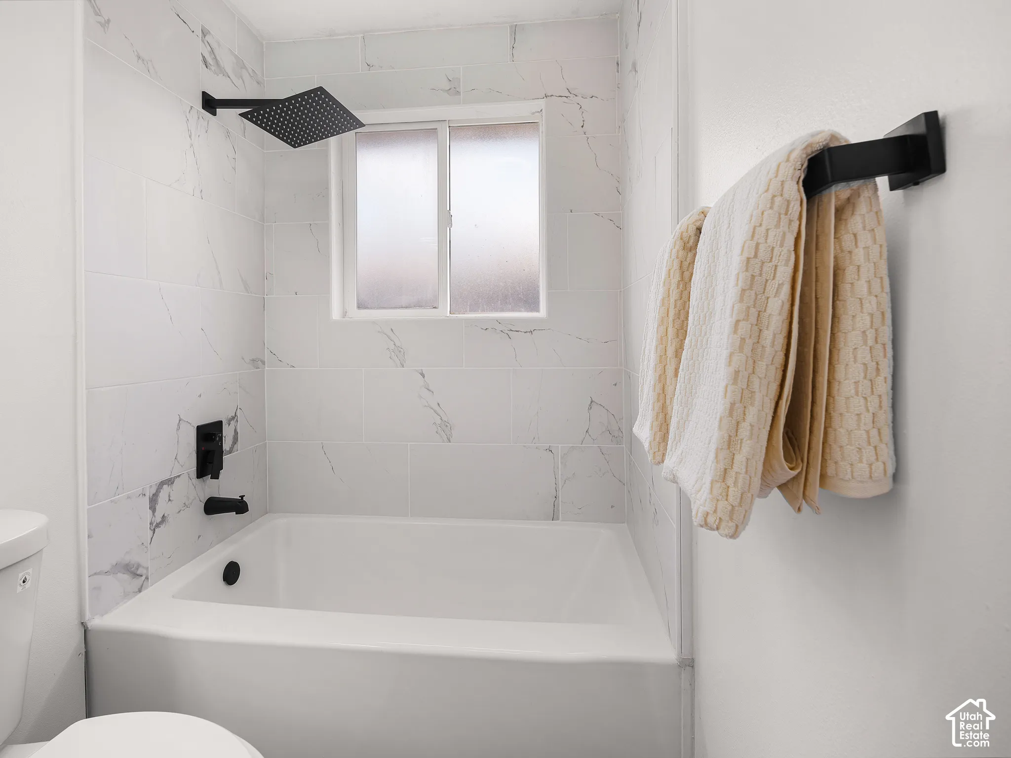 White subway tile surround with subtle veining, matte black rain shower head, built-in bathtub, and obscured window