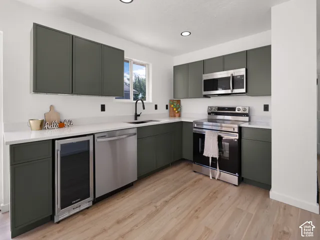 Contemporary kitchen featuring olive-toned cabinetry, light-toned countertops, wood-finish flooring, and stainless steel appliances, including a built-in beverage cooler