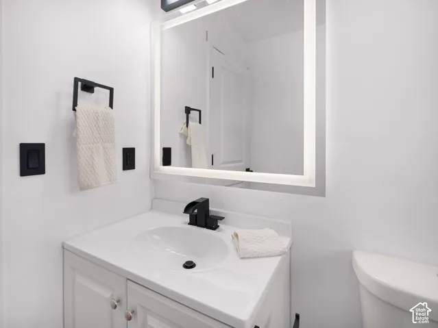 White vanity with a single basin sink, matte black waterfall faucet, and an illuminated mirror
