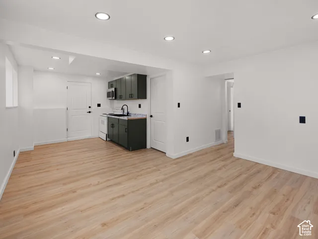 Open-concept living space with wood-finish flooring, recessed lighting, and a compact kitchen featuring dark cabinetry and a built-in microwave