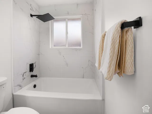 White subway tile surround with subtle veining, matte black rain shower head, built-in bathtub, and obscured window